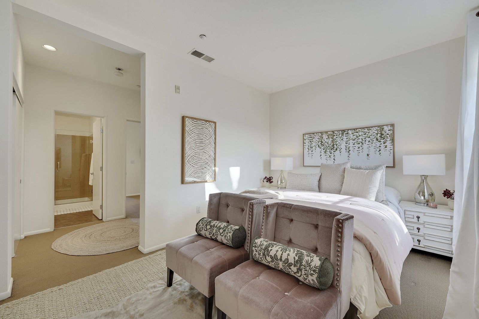 Elegant bedroom with a large bed, two velvet benches at the foot, and symmetrical nightstands with white lamps.