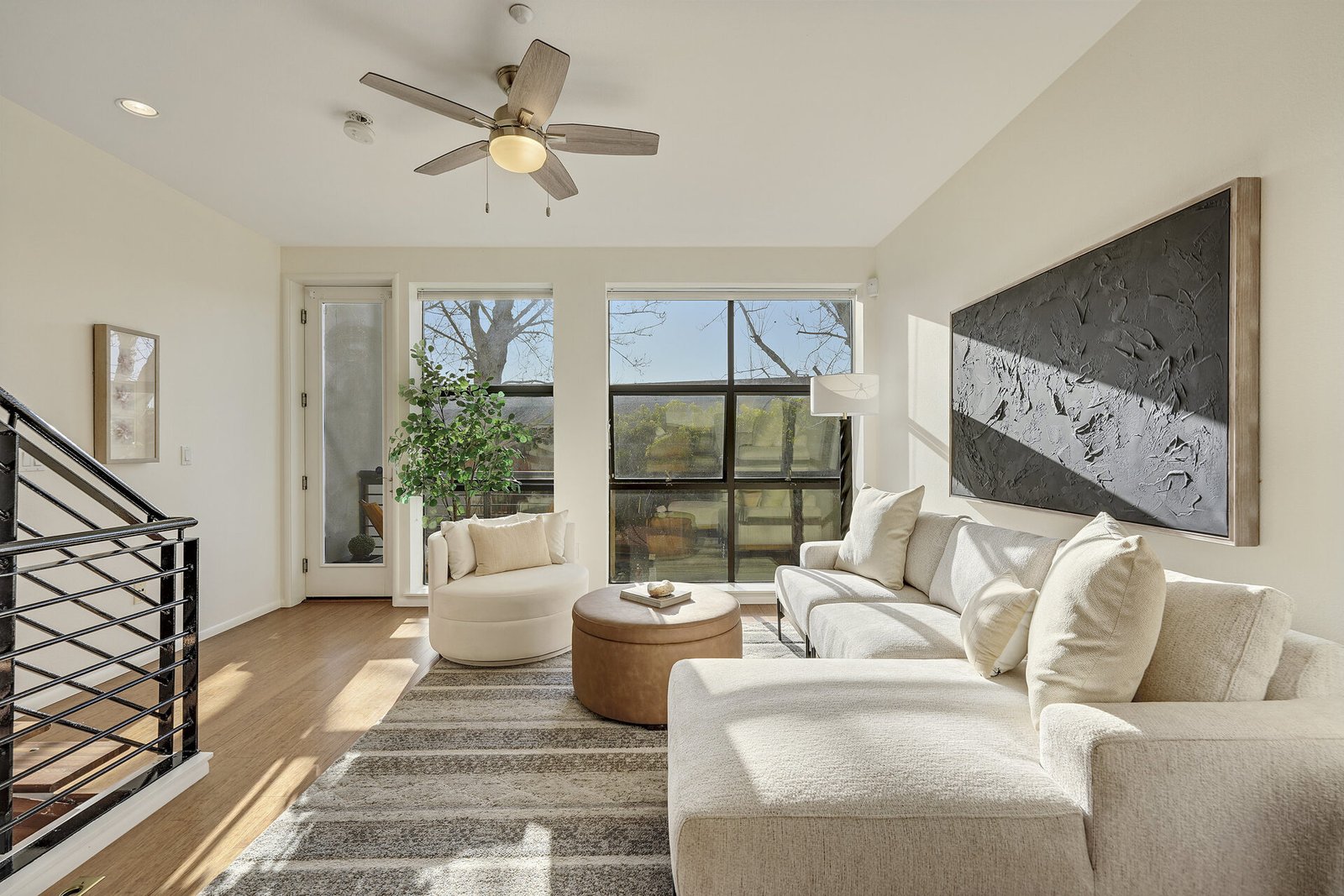 Living room featuring a large white l-shaped sofa, a round leather ottoman, and a large black textured art piece on the wall.